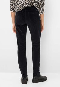 Pantalons en velours côtelé noir à coupe slim, avec des poches arrière et une texture douce, associés à des bottines noires.