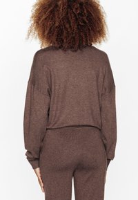 Pull en tricot marron à coupe décontractée, col rond et manches ballons. Assorti avec un pantalon en tricot marron pour un look cohérent.