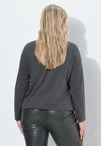 Donkergrijze lange mouw top met een relaxte pasvorm, gecombineerd met glanzende zwarte broek. De stof lijkt soepel en lichtgewicht te zijn, met minimale details.