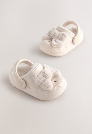 Sabots en caoutchouc beige clair avec nœuds en peluche beige, design texturé, doublure intérieure et trous de ventilation latéraux ; bride réglable incluse.