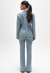 Jasnoniebieski dżinsowy garnitur z dopasowaną marynarką i spodniami dzwonami. Charakteryzuje się dopasowanym krojem, widocznym ściegiem i strzępionymi brzegami spodni.