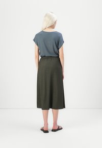 T-shirt i skifergrå med rullede ærmer, parret med en olivenfarvet, ankellang nederdel med elastisk talje. Sorte flip-flops.