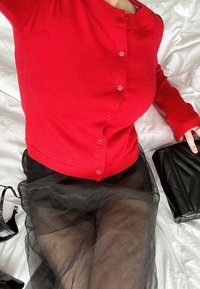 Punane kudumiskardigan nööpidega, kombineeritud läbipaistva musta tüllseelikuga. Aksessuaarideks on must käekott ja mustad kingad.