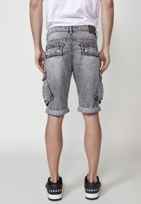 Shorts cargo en denim gris avec des ourlets repliés, deux poches arrière et des poches latérales. Portés avec des baskets noires avec des semelles blanches.