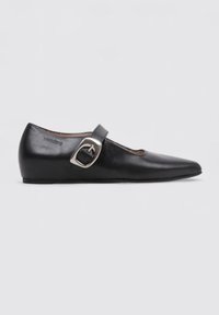 Zapato plano de cuero negro con puntera afilada, que presenta una correa lateral y un detalle de hebilla plateada en la parte superior. Textura suave y diseño minimalista.