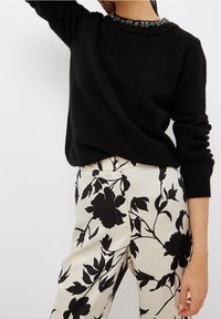 Zwarte, gebreide trui met een gestructureerde halslijn, gecombineerd met crèmekleurige broek met een zwart bloemmotief en een gladde afwerking.