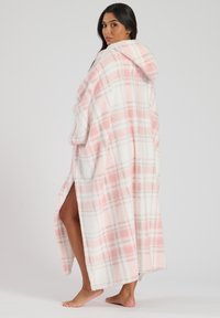 Coperta oversize con cappuccio a quadri rosa e bianca, caratterizzata da una consistenza morbida e fessure laterali per facilitare il movimento, che arriva a metà polpaccio.