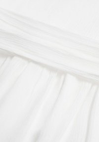 Vitt tyg med en texturerad yta och mjuka plisseringar, samt en slät midja som skapar ett lätt och flödande utseende.