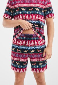 Rode en marineblauwe pyjamset met een patroon van wintermotieven zoals bomen en teckels. Gemaakt van zachte stof en voorzien van een elastische tailleband.