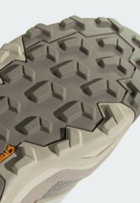 Jasnoszara podeszwa buta trekkingowego z wyraźnym sześciokątnym bieżnikiem, teksturowana powierzchnia oraz szczegół z pomarańczowym logo "Continental". Trwały materiał.