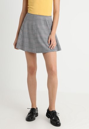 Jupe à carreaux gris avec un design évasé, fabriquée en tissu léger, dotée de subtils accents rouges et d'une texture lisse. Chaussures noires à lacets.