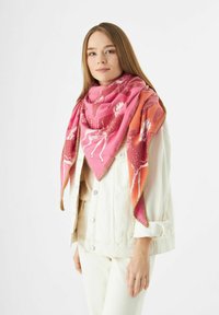Écharpe en tissu doux aux motifs rose et orange, avec un bord frangé et des motifs floraux. Portée en tant que châle triangulaire.