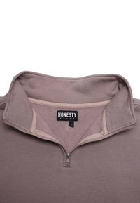 Vaaleanliila puolivetoketjullinen behuone, jossa on fleecevuori, ribbbattu rakenne ja kontrastivärinen kaulus. Varustettu vetoketjulla ja tarralapulla.