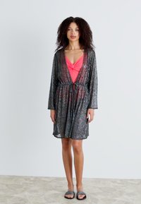 Musta läpinäkyvä kimono-tyylinen peittely, jossa on pitkät hihat, elastinen vyötärö ja sidontakiinnitys; käytetään vaaleanpunaisen uimapuvun päällä. Teksturoitu kangas, jossa on hienovarainen kiilto.