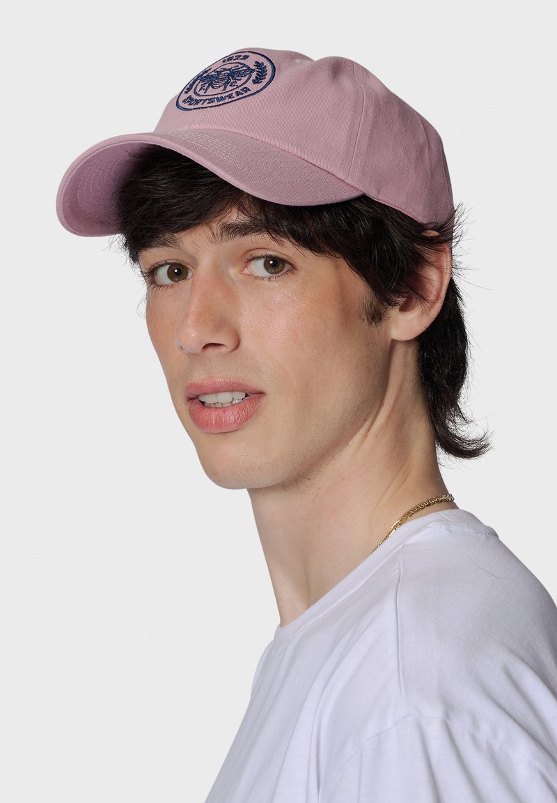 Rosa bomull-basebollkeps med en marinblå broderad logotyp framtill. Har en böjd skärm och justerbart spänne på baksidan.