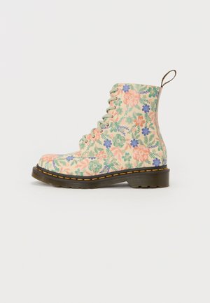 Botte montante à lacets avec fond beige et motif floral pastel en rose, vert et bleu, avec une semelle épaisse noire et des coutures jaunes.