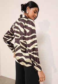 Pika-särg sujuva kangaga, millel on pruun ja kreemjas zebra triibumuster, nööbid mansettide ja krae peal.