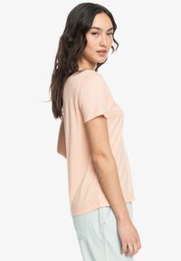Camiseta de manga corta color rosa claro con cuello redondo y textura suave, combinada con pantalones azul claro.