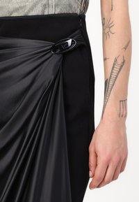Black skirt featuring a draped satin overlay secured with a black clasp. The fabric has a smooth texture with a contrasting ribbed waistband.