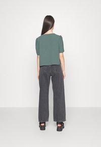 Haut vert à manches courtes avec un col carré, associé à un jean noir taille haute à jambes larges. Conçu avec des manches bouffantes et une finition texturée.