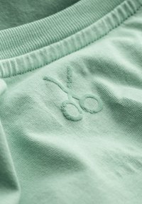 Lichtgroene stof met een gestructureerd oppervlak, met een geborduurd schaarontwerp in een bijpassende kleur. Zacht, casual materiaal.