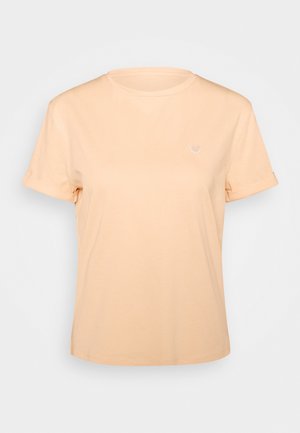 T-shirt à manches courtes couleur pêche clair avec revers roulés et un petit motif de cœur blanc sur la poitrine gauche, présenté sur un fond uni.