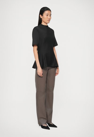 Top negru peplum cu mâneci scurte și guler înalt, asociat cu pantaloni largi gri-maro și tocuri negre ascuțite. Textură de țesătură netedă.