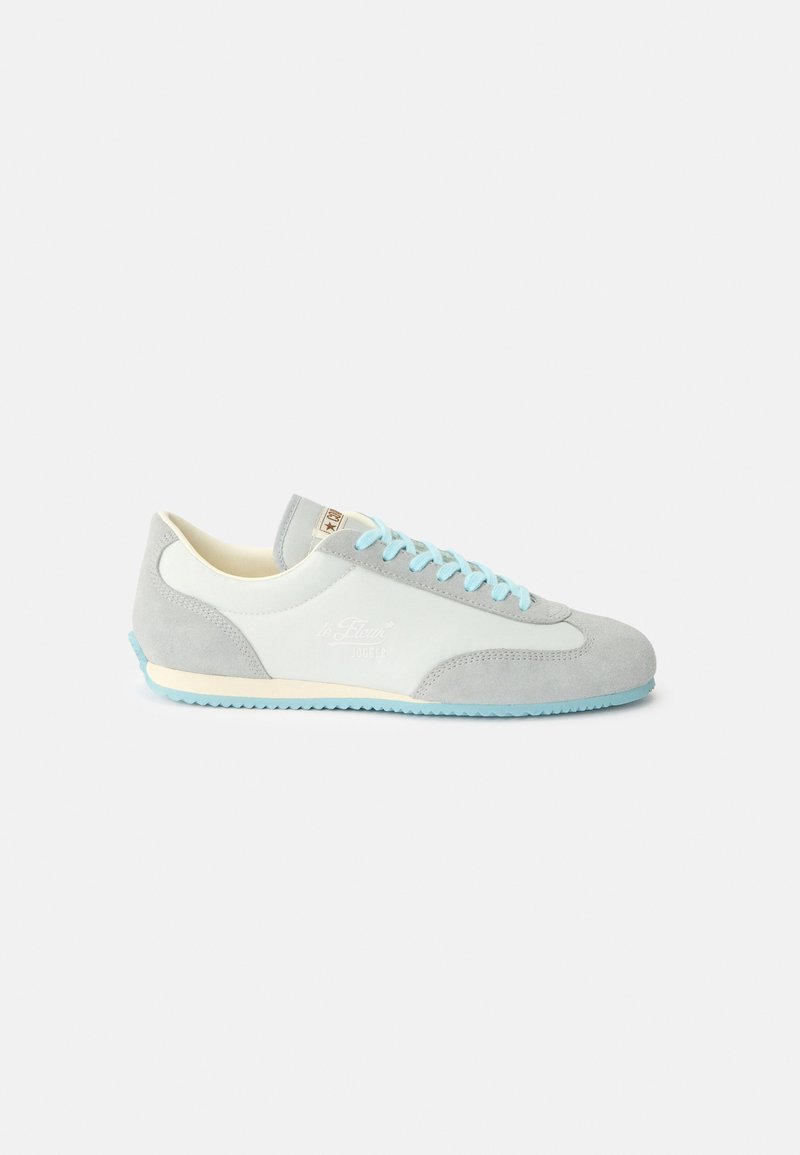 Sneaker basso grigio chiaro e bianco con lacci e suola blu, dettagli in camoscio e suola esterna strutturata.