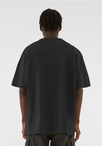 Schwarzes übergroßes T-Shirt mit Rundhalsausschnitt, kurzen Ärmeln und lockerer Passform. Der Stoff wirkt weich mit einer dezenten Textur.