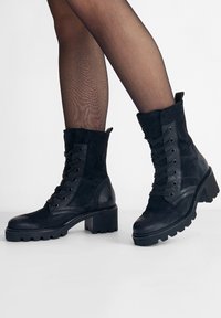 Černé kotníkové boty kombinující hladkou kůži a semiš, šněrování vpředu, kulatá špička a robustní, strukturovaná podešev.