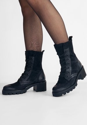 Černé kotníkové boty kombinující hladkou kůži a semiš, šněrování vpředu, kulatá špička a robustní, strukturovaná podešev.