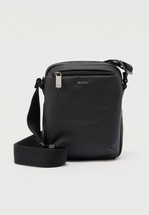 Kompaktowa czarna torba na ramię z regulowanym paskiem, przednią kieszenią na zamek oraz metalowym logo „BOSS” na gładkiej powierzchni.