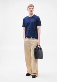 Μπλε ναυτικό βαμβακερό μπλουζάκι με διακριτή υφή, μπεζ παντελόνι φαρδιάς γραμμής, μαύρη δερμάτινη τσάντα με κοντά χερούλια και μαύρα παπούτσια.