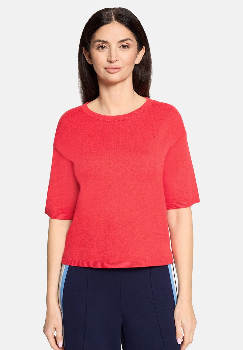 Pull rouge à manches courtes avec un col rond et un ourlet côtelé. Texture douce et coupe décontractée, présenté avec un pantalon bleu marine à rayures latérales.