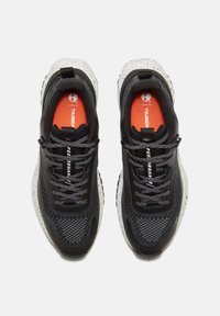 Svarta sportskor med övre del av grått mesh, prickig vit mellansula och orange innersulor. Har svarta snören och tryckt varumärke.