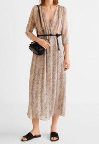 Pitkä, beige mekko, jossa on käärmeennahkakuosi, syvä V-mallinen kaula-aukko, kolmanneksen pituiset hihat ja musta vyö. Yhdistetty mustiin litteisiin sandaaleihin ja pieneen laukkuun.