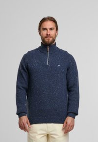 Marineblauer Strickpullover mit hohem Kragen und halbem Reißverschluss, ausgestattet mit einem strukturierten Design und kleinem Logo auf der Brust.