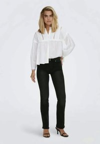 Bijela pamučna bluzica s vertikalnim prugama i dugmadi, uparena s uskim crnim trapericama i crnim sandalama s visokom potpeticom.