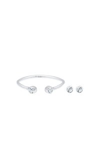 Anello in argento sterling con due cristalli trasparenti rotondi a ciascun estremo, accompagnato da due orecchini a bottone abbinati con un design di cristallo simile.