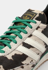 Adidas sneakers with cowhide upper, featuring a black and white pattern, green laces, and white leather stripes. Textured rubber outsole.