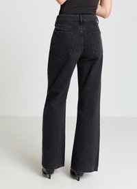 Jean denim noir à jambes larges avec une taille haute, comportant deux poches arrière, des coutures discrètes et une surface légèrement texturée.