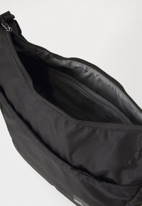Svart stoffbag med glidelås, preget av en jevn tekstur og et indre rom. Inkluderer en frontlomme med logo.