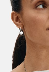 Hõbedast rõngaskõrvarõngas südamekujuga ripatsiga. Ripats on läikiva viimistlusega ja peegeldava pinnaga. Lihtne ja kaasaegne disain.