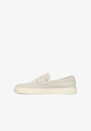 Lichtbeige suède loafer met een lage rubberen zool en een riemdetail over het bovenwerk, zijaanzicht op een witte achtergrond.