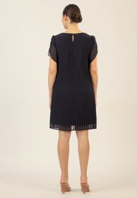 Navyblaues Kleid mit plissiertem Rock und durchsichtigen Ärmeln, mit einem Schlüssellochverschluss mit Knopf im Rücken und einem knielangen Saum.