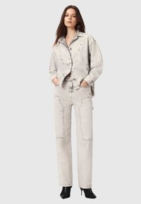 Jasnoszara kurtka i spodnie dżinsowe, charakteryzujące się luźnym krojem, widocznym szwem i kieszeniami z łatami; model nosi botki na obcasie.