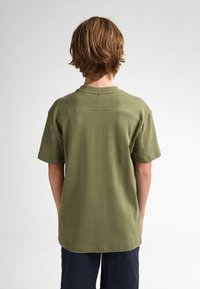 Camiseta de algodón verde oliva con mangas cortas, escote redondo y corte relajado. Presenta una textura suave y detalles de costura mínimos.