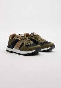 Zapatillas deportivas con una combinación de colores en verde oliva, negro y beige. Materiales de malla y ante; suela acolchada con agarres texturizados.