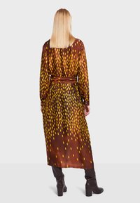 Lunga gonna in seta con una base marrone e motivi rettangolari gialli, con cintura in vita e maniche lunghe con dettagli dei bottoni.