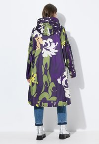 Paarse bloemenregenjas met een overgrote capuchon, versierd met grote witte en groene patronen. Draag het over blauwe jeans en zilveren chelsea boots.